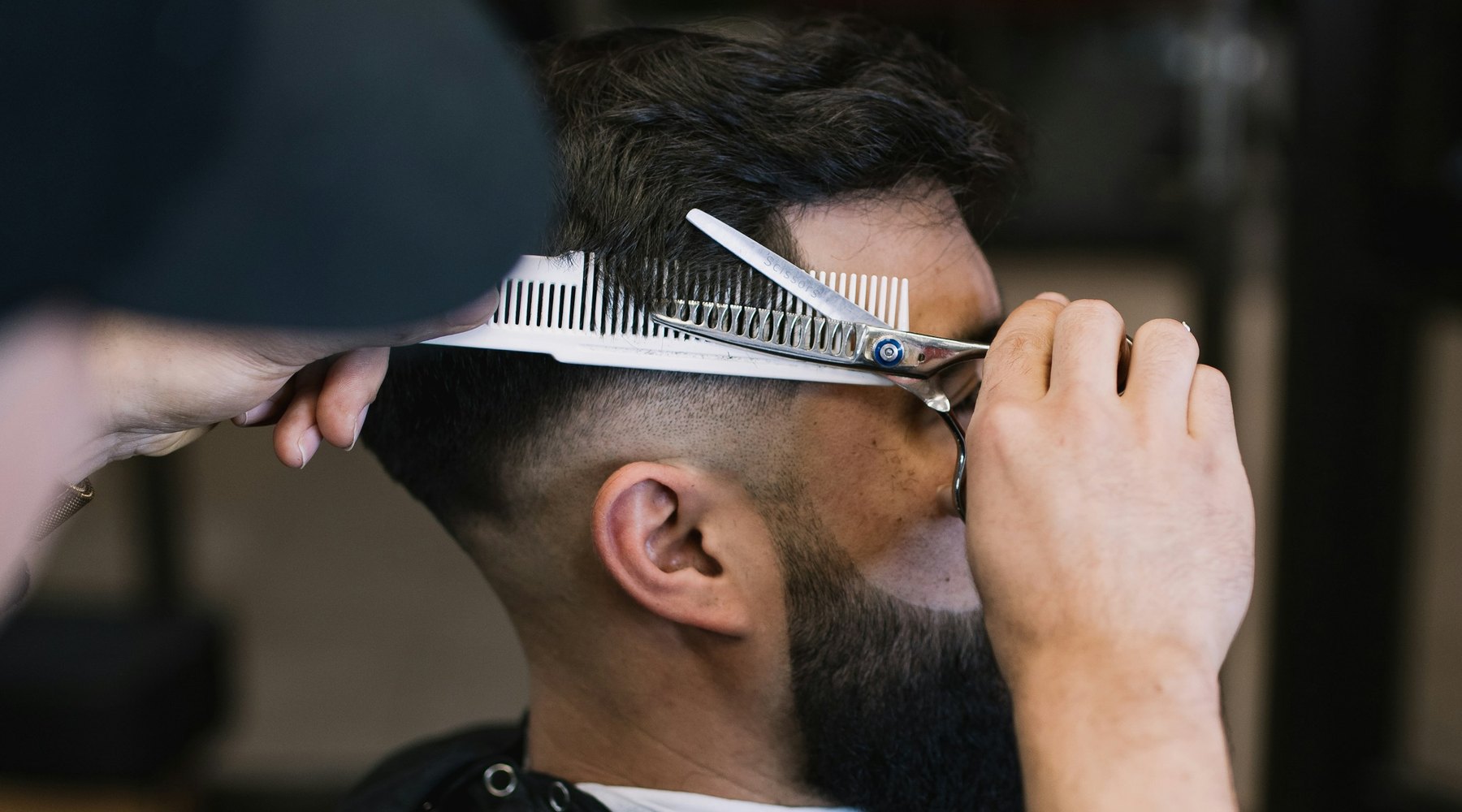 A comb held flat against the side of a client's head with thinning shears part-way through the cut